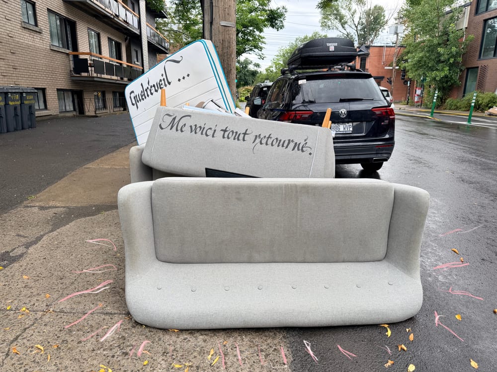 Discarded couches and mattresses on street with hand-painted text signage.